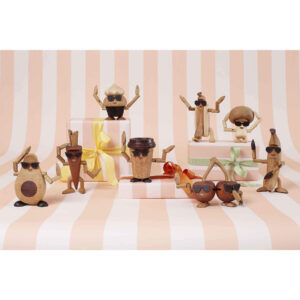 Flera glada träfigurer i form av frukter, kaffe, grönsaker och bakverk poserar med solglasögon mot randig bakgrund och presentaskar.